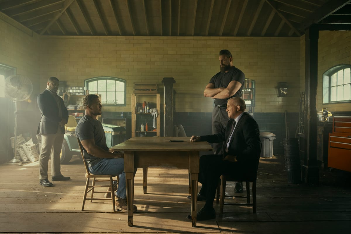 Reacher season 3: Paulie stands with arms crossed over Jack Reacher and Zachary Beck at a table in a garage